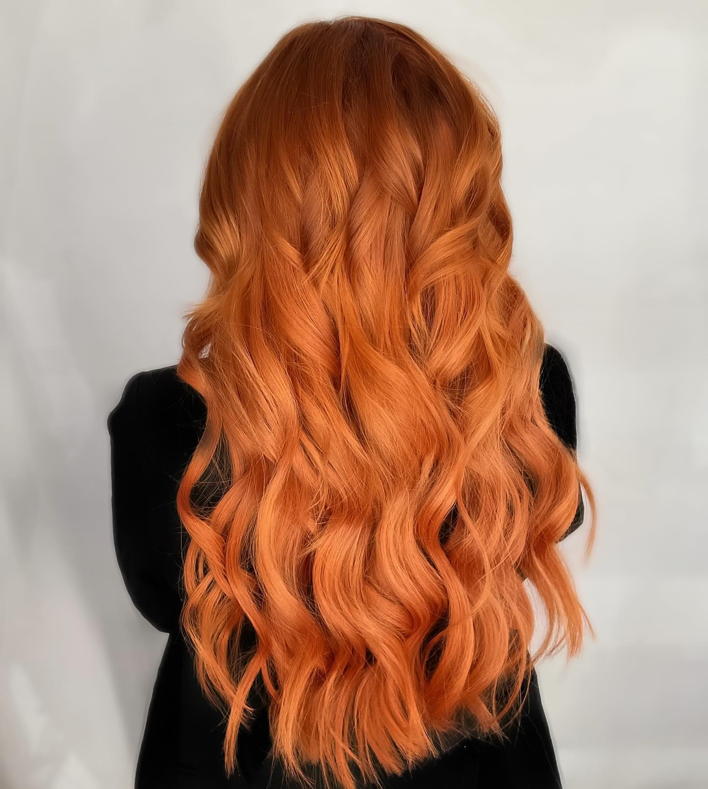Long copper hair styled in flowing waves against a pale background