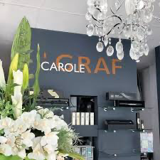 The salon's copper Carole Graf sign on a charcoal wall, with white flowers and a chandelier